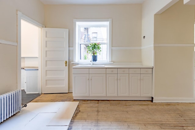 668 W Irving Park Rd Unit H1, Chicago, IL 60613 - kitchen with radiator, light wood-style flooring, light countertops, and white cabinets