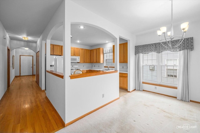 1909 Lakeside Dr, Montgomery, IL 60538 - kitchen featuring white appliances, arched walkways, a chandelier, brown cabinetry, and decorative light fixtures