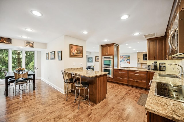 1740 Mission Hills Rd Unit 304, Northbrook, IL 60062 - kitchen with stainless steel appliances, a peninsula, a breakfast bar area, light wood-style flooring, and light stone counters