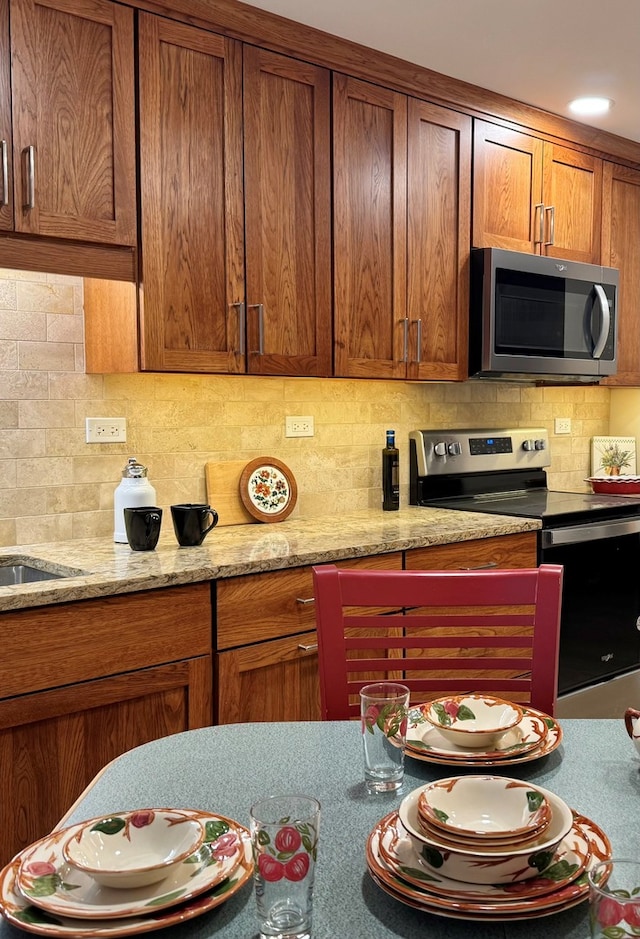 825 Pearson St Unit 3A, Des Plaines, IL 60016 - kitchen featuring stainless steel appliances, decorative backsplash, brown cabinets, and light stone countertops