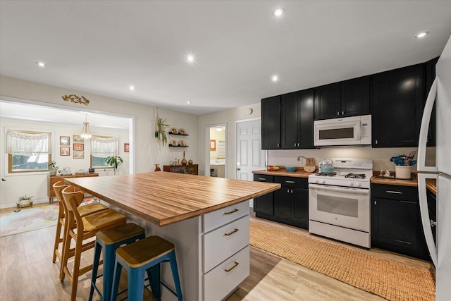 1704 Chevy Chase Dr, Champaign, IL 61821 - kitchen featuring white appliances, dark cabinetry, butcher block countertops, a breakfast bar, and light wood-style flooring