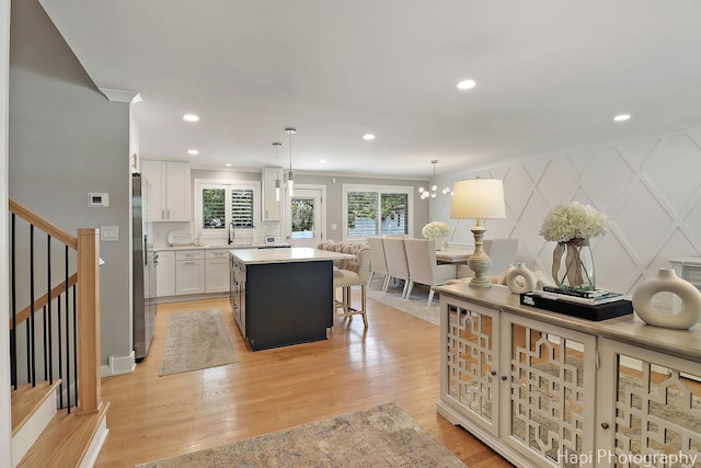 813 E Gardenia Ln, Palatine, IL 60074 - kitchen with stainless steel fridge, a kitchen island, white cabinets, a breakfast bar, and light wood-type flooring