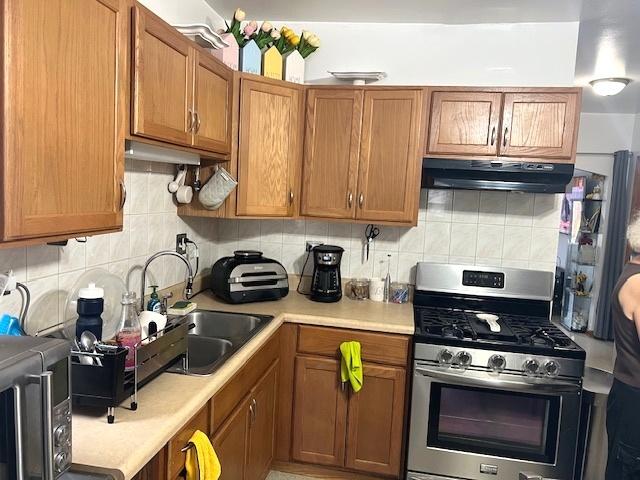 5536 S Albany Ave, Chicago, IL 60629 - kitchen with stainless steel gas range oven, under cabinet range hood, light countertops, decorative backsplash, and brown cabinetry