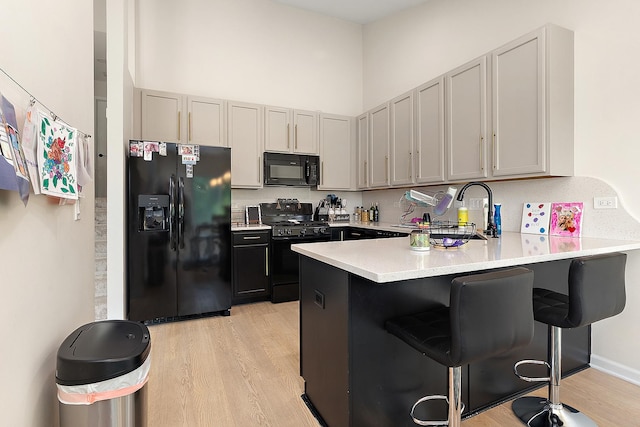 1602 Peachtree Ln, Lockport, IL 60441 - kitchen with black appliances, a peninsula, light wood-style flooring, a kitchen breakfast bar, and light countertops