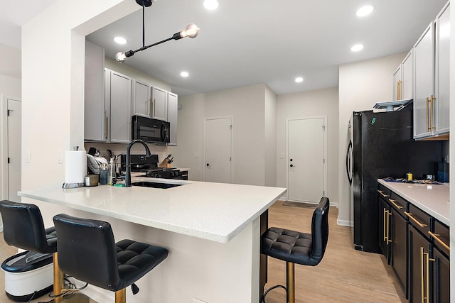 1528 Peachtree Ln, Lockport, IL 60441 - kitchen featuring black microwave, stove, light wood-style flooring, a peninsula, and a kitchen bar
