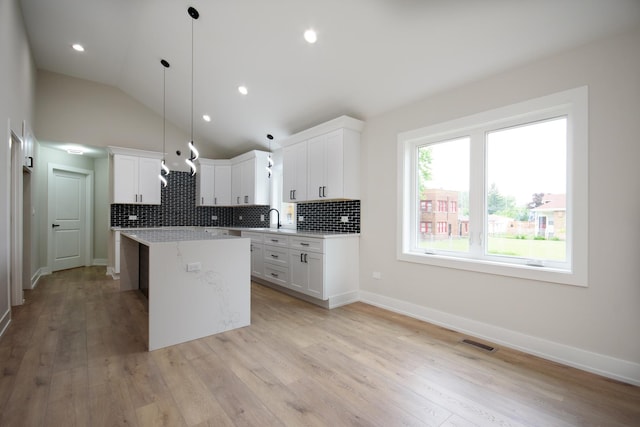 8402 S Carpenter St, Chicago, IL 60620 - kitchen featuring a center island, backsplash, light wood-style floors, white cabinetry, and lofted ceiling