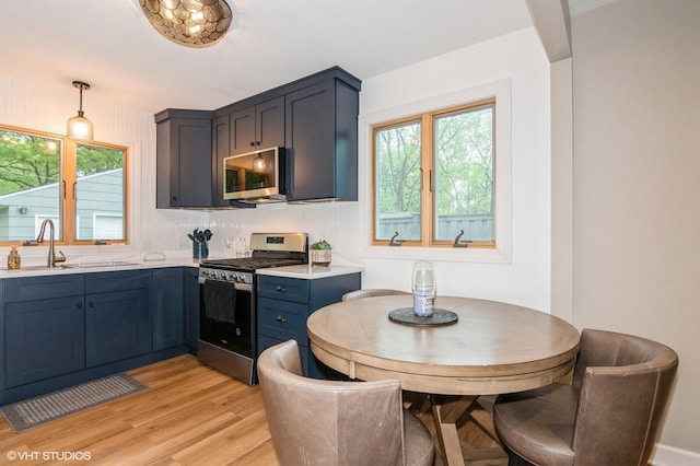 2365 N Barrington Woods Rd, Palatine, IL 60074 - kitchen with appliances with stainless steel finishes, light countertops, light wood-style flooring, blue cabinetry, and hanging light fixtures