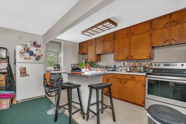 107 N Elm St, Gardner, IL 60424 - kitchen featuring freestanding refrigerator, stainless steel electric range oven, backsplash, brown cabinetry, and light countertops