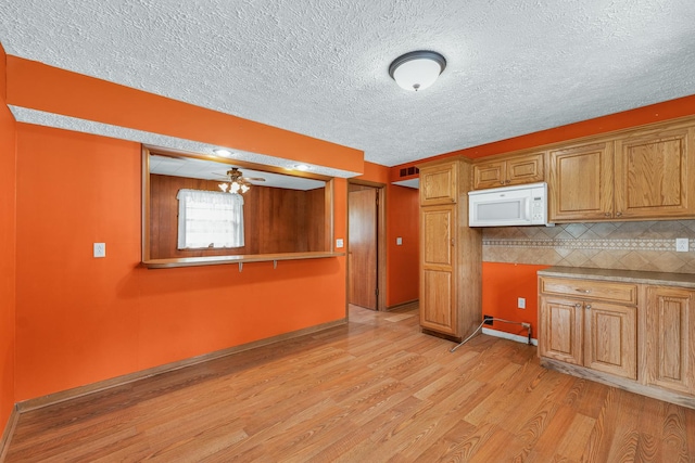 319 N Third St, Fisher, IL 61843 - kitchen with white microwave, light wood finished floors, a textured ceiling, decorative backsplash, and brown cabinetry
