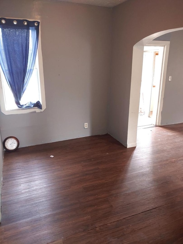 spare room featuring arched walkways and dark wood-style flooring