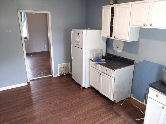 kitchen with dark countertops, dark wood finished floors, freestanding refrigerator, and white cabinetry