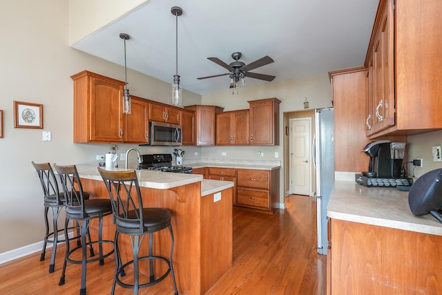 236 Marquette Pl S, Manteno, IL 60950 - kitchen featuring stainless steel appliances, a peninsula, a ceiling fan, brown cabinets, and light wood-style floors