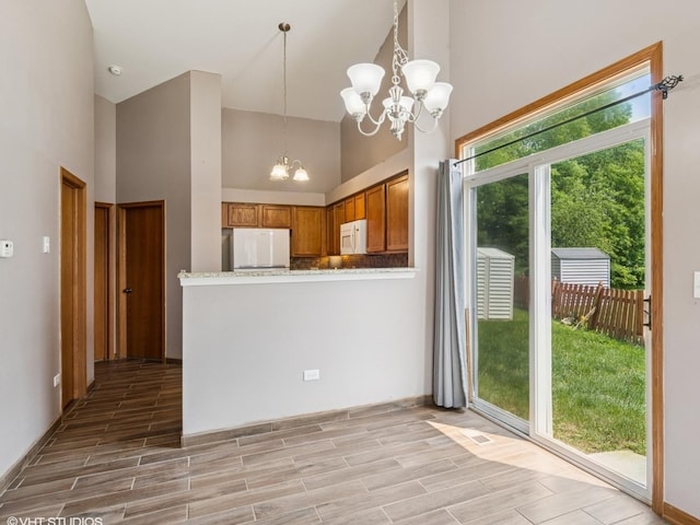 722 Eberly Ct, Plano, IL 60545 - kitchen with a chandelier, refrigerator, white microwave, brown cabinetry, and high vaulted ceiling