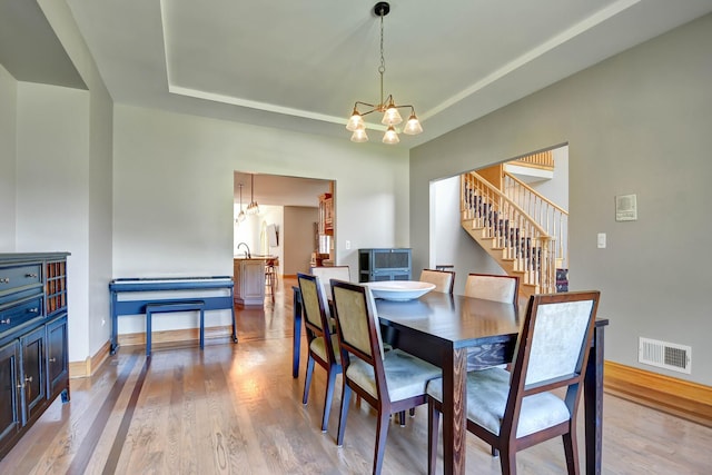 1383 Gordon Ln, Lemont, IL 60439 - dining room featuring a chandelier, light wood finished floors, a tray ceiling, and stairway