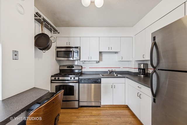 2144 N Lincoln Park W Unit 23B, Chicago, IL 60614 - kitchen featuring appliances with stainless steel finishes, dark countertops, white cabinets, backsplash, and light wood-style flooring