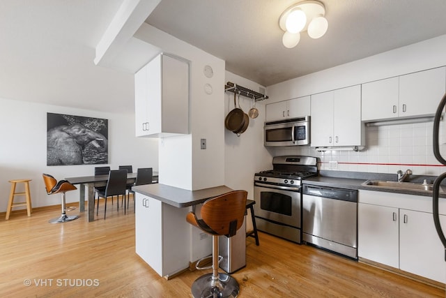 2144 N Lincoln Park W Unit 23B, Chicago, IL 60614 - kitchen with stainless steel appliances, dark countertops, tasteful backsplash, white cabinets, and a kitchen bar