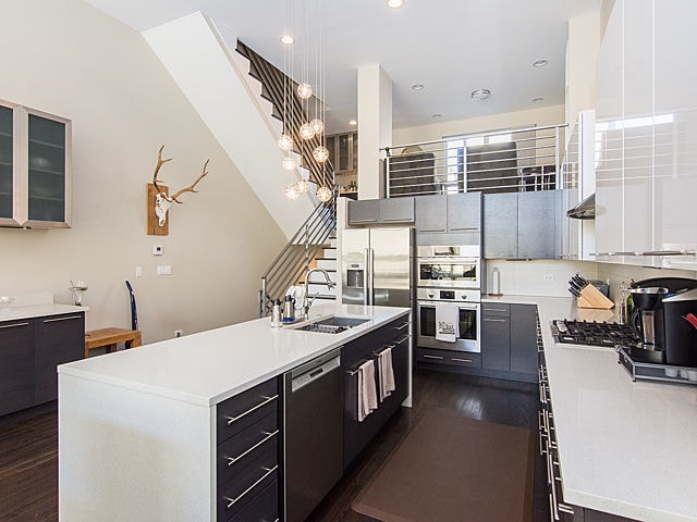 2036 W Huron St, Chicago, IL 60612 - kitchen featuring appliances with stainless steel finishes, dark wood-style flooring, light countertops, a center island with sink, and glass insert cabinets