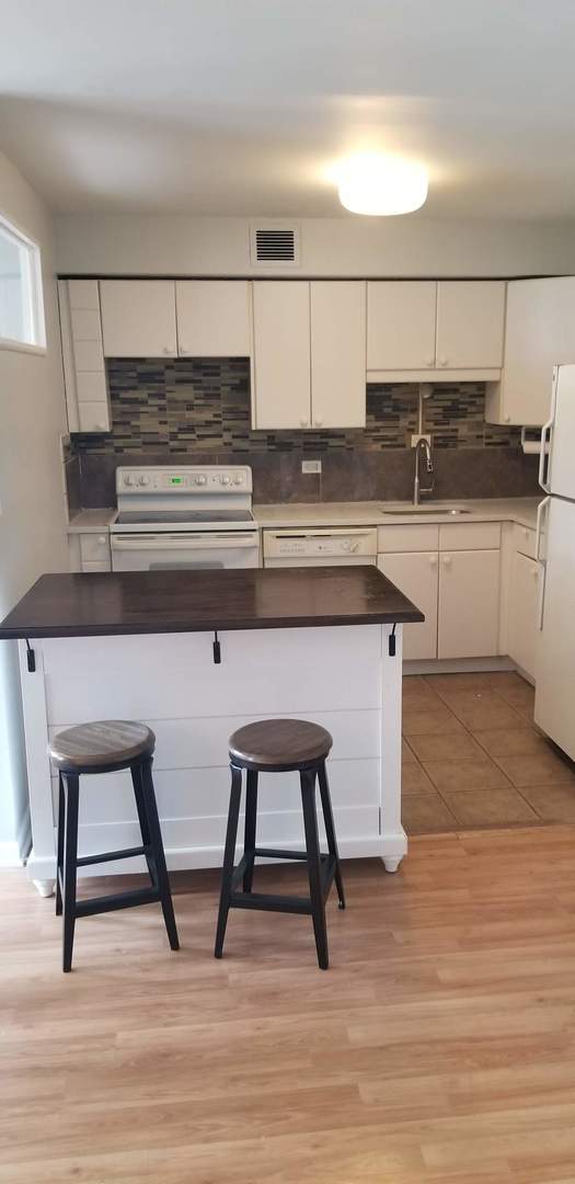 6300 N Sheridan Rd Unit 107, Chicago, IL 60660 - kitchen with white appliances, white cabinets, tasteful backsplash, a kitchen bar, and light wood-style flooring