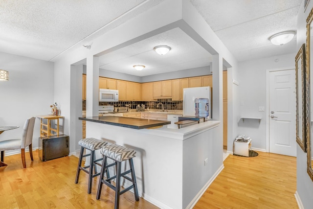 6807 N Milwaukee Ave Unit 411, Niles, IL 60714 - kitchen featuring white appliances, a textured ceiling, light brown cabinets, light wood-style flooring, and a kitchen breakfast bar