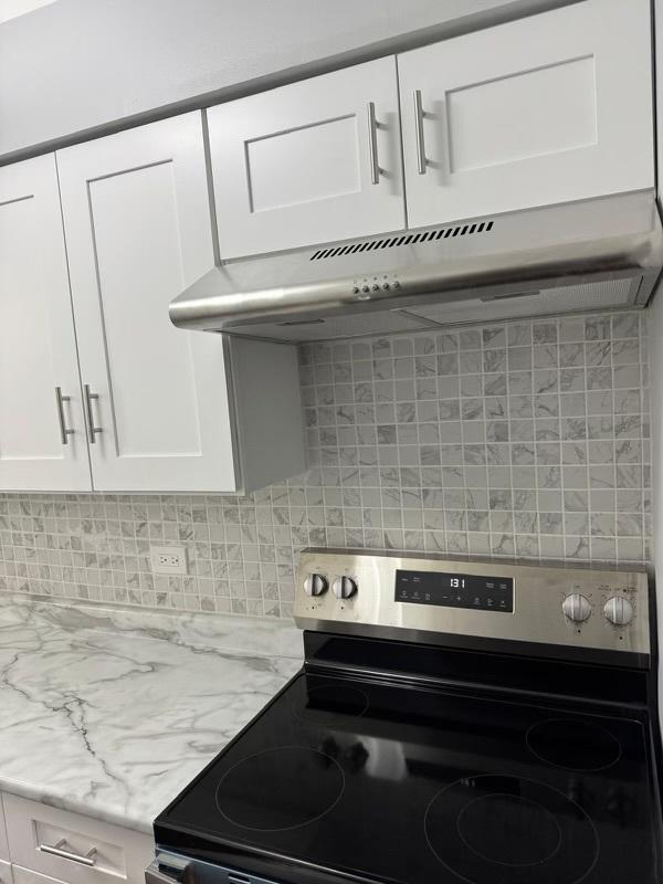 5204 Midlothian Tpke Unit 222, Crestwood, IL 60418 - kitchen with stainless steel range with electric cooktop, white cabinets, backsplash, under cabinet range hood, and light stone counters