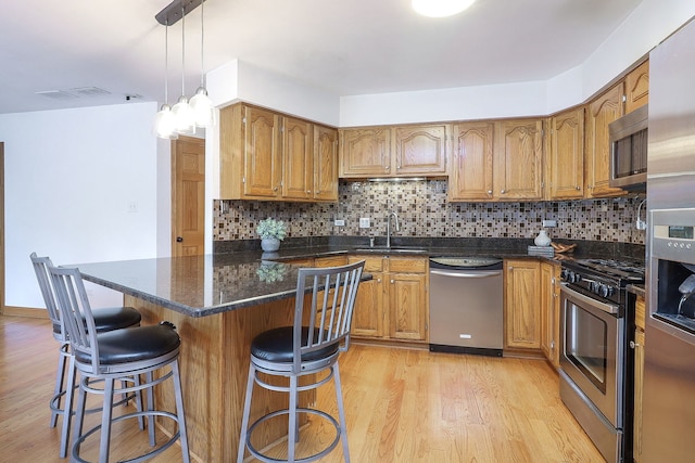5135 W 113th Pl, Alsip, IL 60803 - kitchen with appliances with stainless steel finishes, light wood finished floors, a breakfast bar area, brown cabinets, and tasteful backsplash