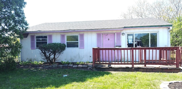 view of front of house featuring a deck, a front lawn, and roof with shingles