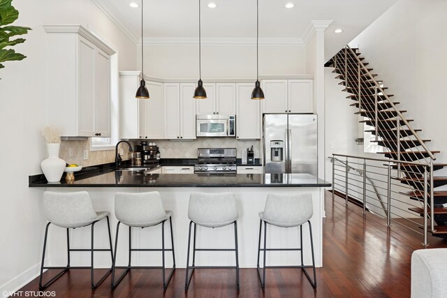 1051 N Hermitage Ave Unit 3, Chicago, IL 60622 - kitchen featuring stainless steel appliances, a peninsula, dark countertops, white cabinetry, and hanging light fixtures