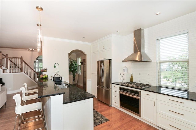 768 W St Johns Pl, Addison, IL 60101 - kitchen featuring appliances with stainless steel finishes, wall chimney exhaust hood, arched walkways, a kitchen bar, and dark stone countertops