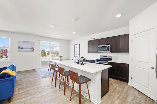 2029 Magnolia Ln, Wonder Lake, IL 60097 - kitchen with appliances with stainless steel finishes, a breakfast bar, light wood finished floors, a kitchen island with sink, and light countertops