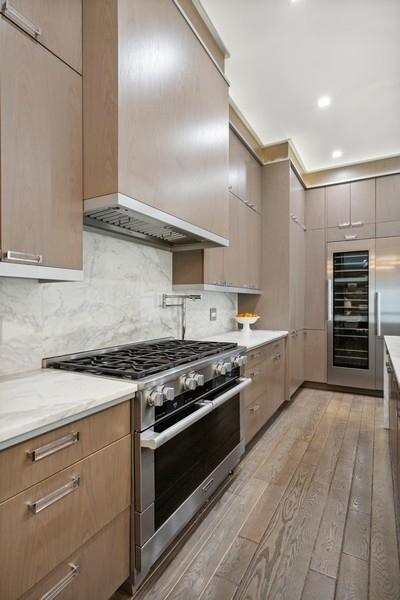 34 E Bellevue Pl, Chicago, IL 60611 - kitchen with high end stove, custom exhaust hood, light wood-style flooring, beverage cooler, and modern cabinets