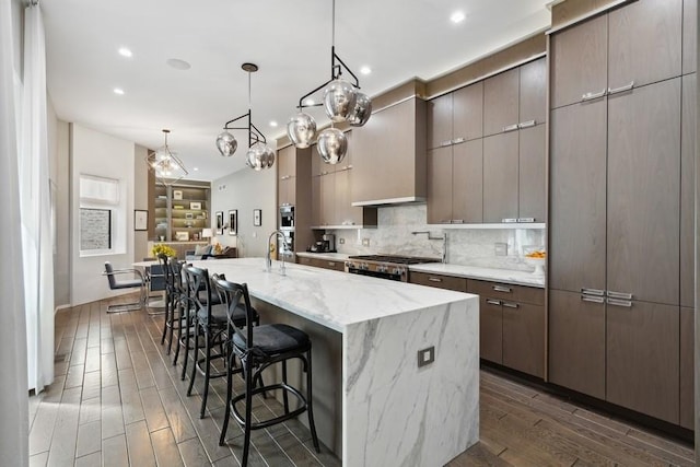 34 E Bellevue Pl, Chicago, IL 60611 - kitchen with dark wood-style floors, tasteful backsplash, an island with sink, stainless steel range oven, and a kitchen bar