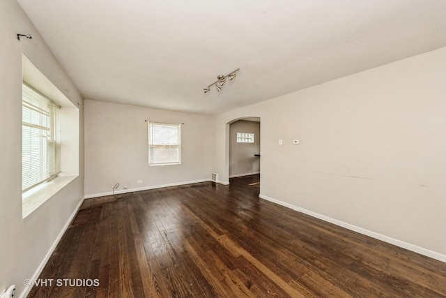 unfurnished room with arched walkways, hardwood / wood-style flooring, and rail lighting