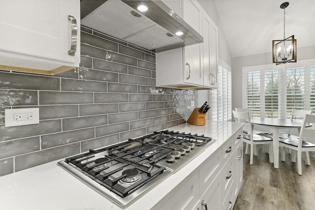 8081 Tennessee Ave, Willowbrook, IL 60527 - kitchen featuring wall chimney range hood, stainless steel gas cooktop, a chandelier, tasteful backsplash, and white cabinetry