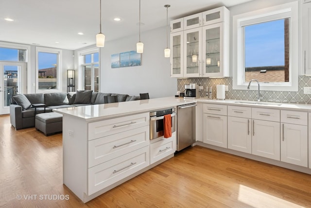 2442 N Clybourn Ave Unit 5S, Chicago, IL 60614 - kitchen with stainless steel appliances, a peninsula, white cabinets, light wood finished floors, and tasteful backsplash