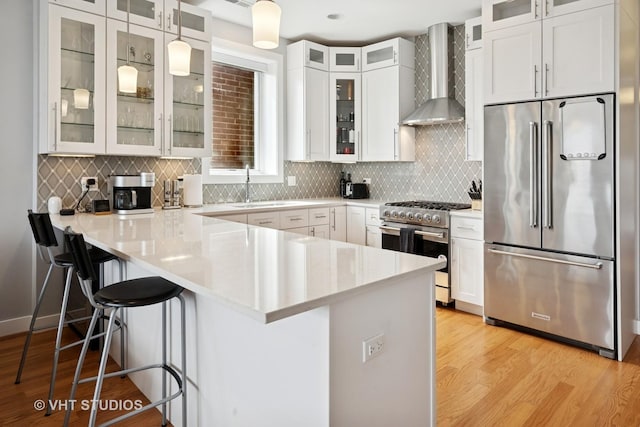 2442 N Clybourn Ave Unit 5S, Chicago, IL 60614 - kitchen with high quality appliances, wall chimney range hood, a peninsula, light wood finished floors, and white cabinetry