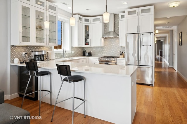 2442 N Clybourn Ave Unit 5S, Chicago, IL 60614 - kitchen with high end appliances, wall chimney exhaust hood, a peninsula, light wood-style flooring, and light countertops