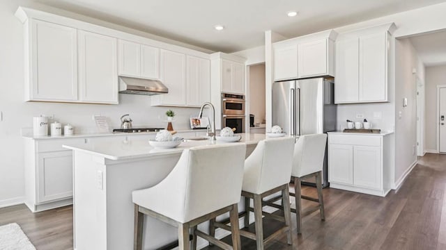 1818 Legacy Pointe Blvd, Plainfield, IL 60586 - kitchen with under cabinet range hood, dark wood finished floors, light countertops, a kitchen island with sink, and white cabinets
