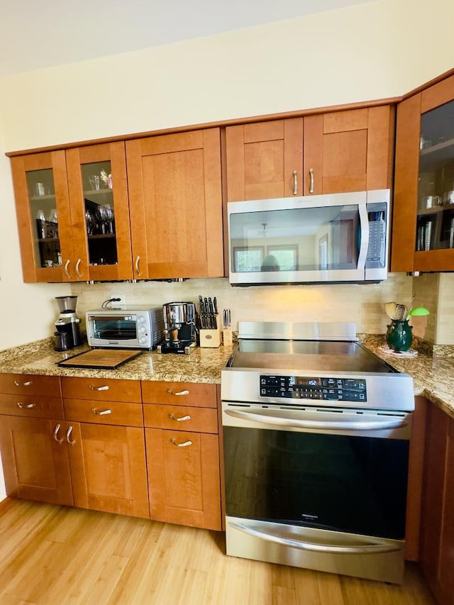 9321 S 81st Ct, Hickory Hills, IL 60457 - kitchen featuring stainless steel appliances, brown cabinets, glass insert cabinets, light wood finished floors, and light stone countertops