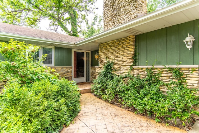 2458 E Cass St, Joliet, IL 60432 - view of exterior entry featuring a chimney, stone siding, roof with shingles, and board and batten siding