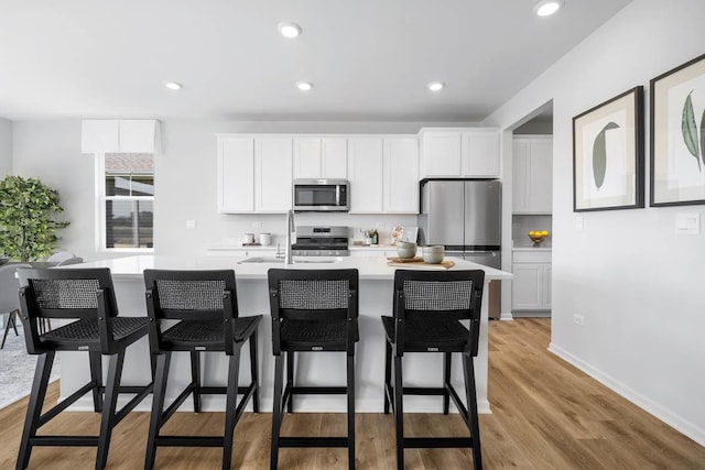 17225 Munster Ln, Tinley Park, IL 60477 - kitchen featuring stainless steel appliances, an island with sink, light countertops, white cabinets, and light wood-style flooring