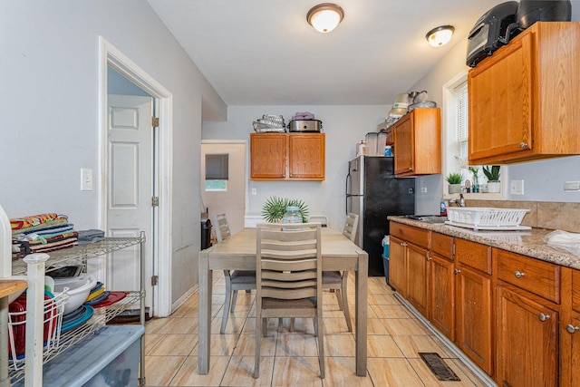 28 W 112th St, Chicago, IL 60628 - kitchen featuring freestanding refrigerator, brown cabinets, light tile patterned flooring, and light stone counters