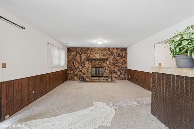unfurnished living room with a wainscoted wall, a stone fireplace, carpet floors, and wooden walls
