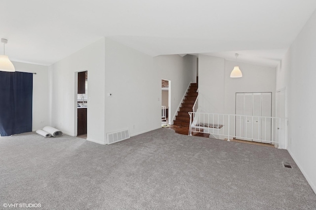 carpeted spare room with stairs and vaulted ceiling