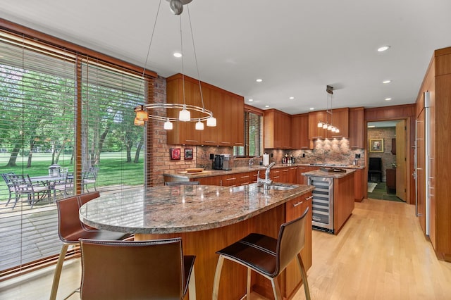 1200 Regency Ln, Lake Forest, IL 60045 - kitchen with an island with sink, wine cooler, brown cabinetry, backsplash, and light wood finished floors