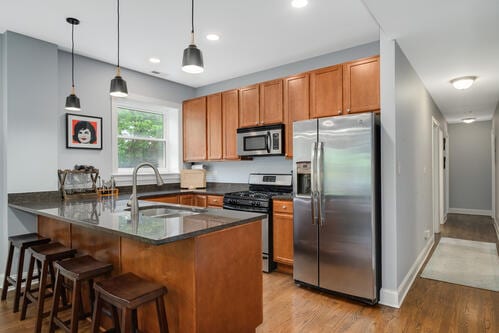 4259 N Ashland Ave Unit 2, Chicago, IL 60613 - kitchen with appliances with stainless steel finishes, a peninsula, light wood-style flooring, hanging light fixtures, and brown cabinets