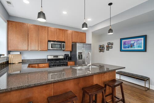 4259 N Ashland Ave Unit 2, Chicago, IL 60613 - kitchen featuring appliances with stainless steel finishes, a peninsula, decorative light fixtures, brown cabinetry, and recessed lighting