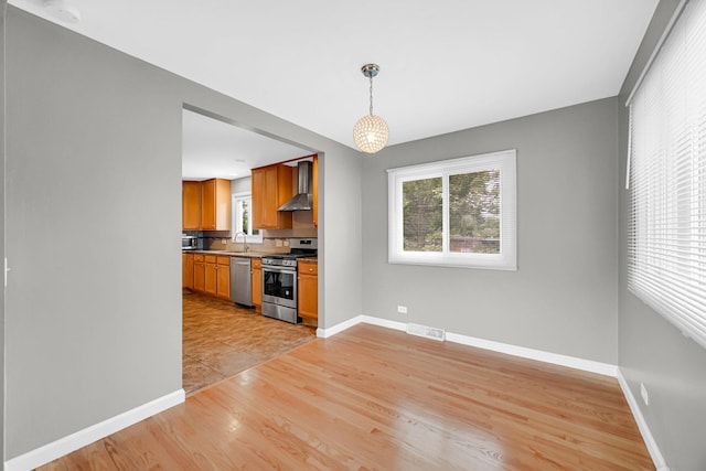 220 N Yates Ln, Mount Prospect, IL 60056 - kitchen featuring stainless steel appliances, wall chimney exhaust hood, light wood-style floors, brown cabinetry, and pendant lighting