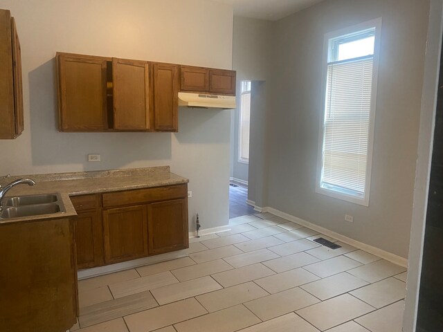 537 W 61st Pl, Chicago, IL 60621 - kitchen featuring under cabinet range hood, brown cabinets, light tile patterned floors, and light countertops