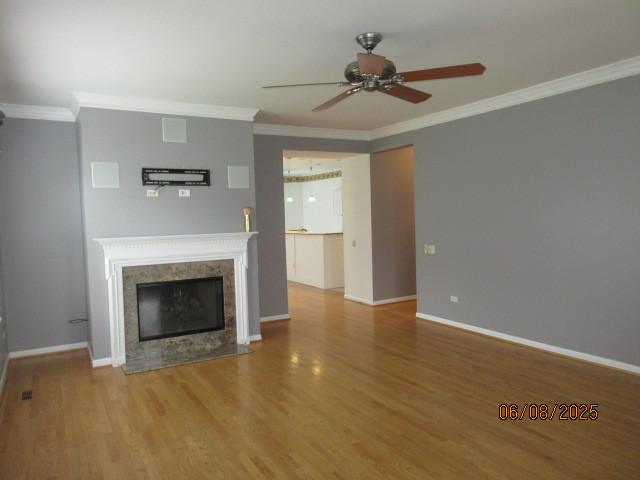 13005 Big Horn Dr, Huntley, IL 60142 - unfurnished living room featuring a ceiling fan, crown molding, wood finished floors, and a tiled fireplace