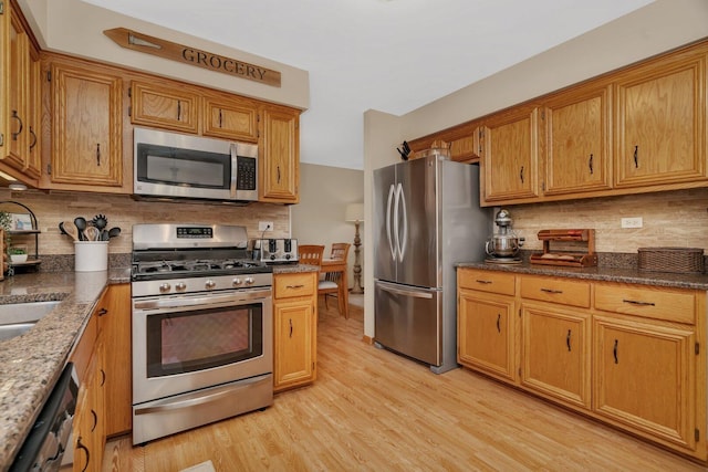 512 Creekside Cir, Minooka, IL 60447 - kitchen featuring appliances with stainless steel finishes, decorative backsplash, light wood finished floors, brown cabinetry, and dark stone countertops